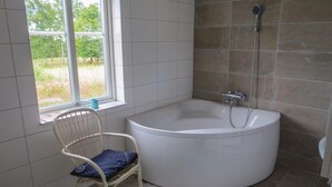 A bathroom with a large bathtub, a window with a view of greenery, and a chair with a cushion. - 4 bedroom beautiful home in Gnosjö (Gnosjö)