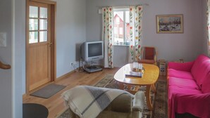A living room with a wooden door, a television, a pink sofa, a table with a book and a candle, and a patterned rug. - 4 bedroom beautiful home in Gnosjö (Gnosjö)