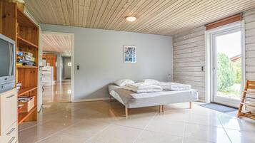 Ein Schlafzimmer mit einem Bett, einem Fernseher, einem Holzschrank und einer Tür zu einem weiteren Raum.