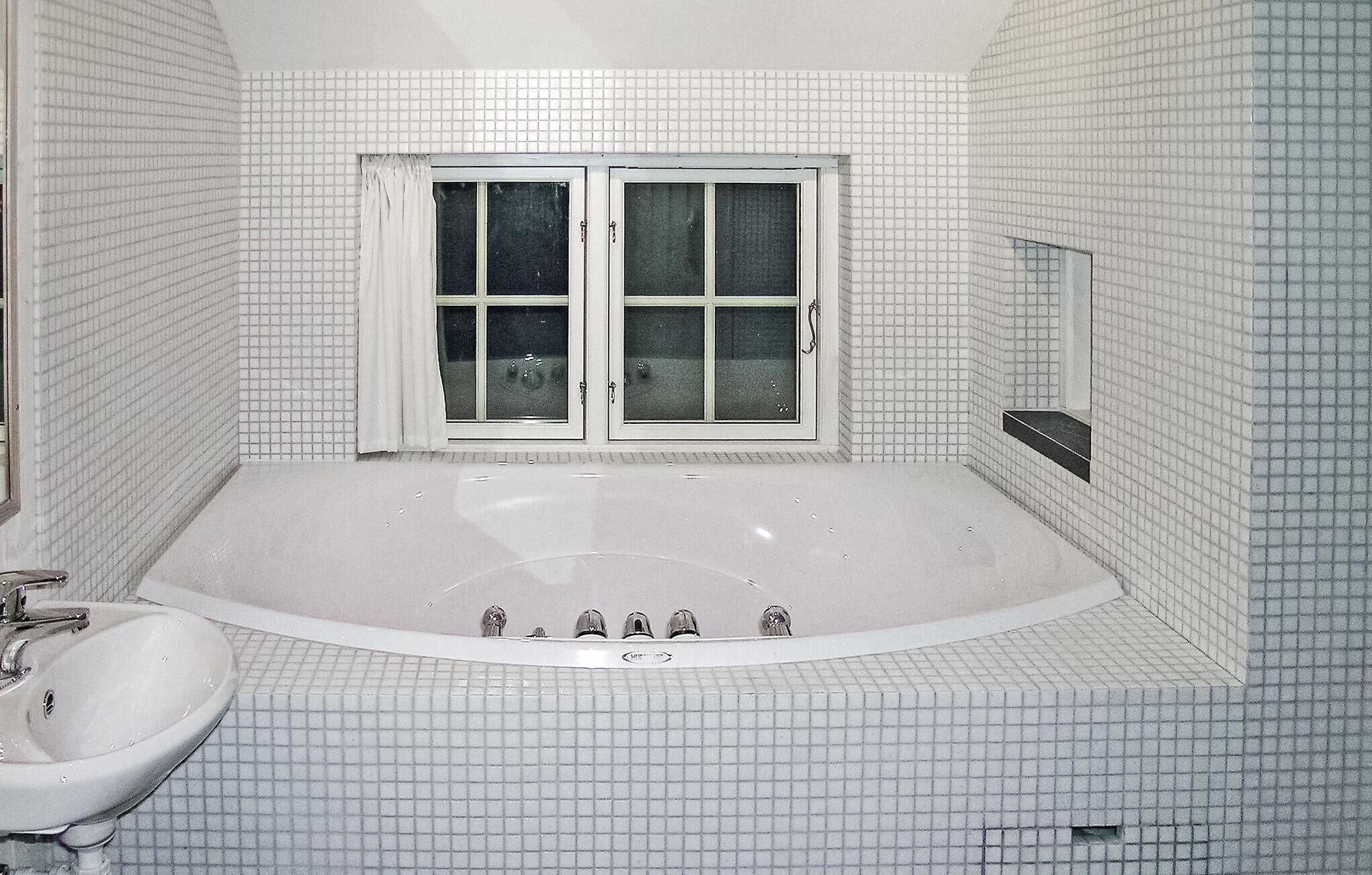 Ein Badezimmer mit einer großen Badewanne, einem Waschbecken und einem Fenster mit Vorhängen.