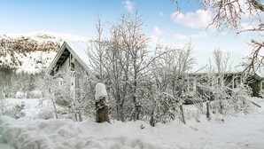Paesaggio innevato con una baita di legno e un albero ricoperto di neve.