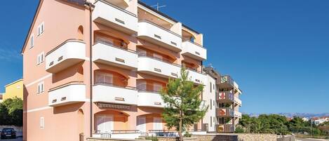 A multi-story residential building with balconies, a stone facade, and a clear sky.