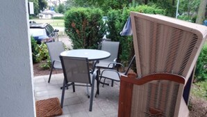 An outdoor patio area with a round table and four chairs, surrounded by greenery.
