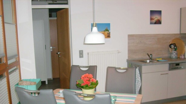 A compact kitchen with a dining area, featuring a table with chairs, a hanging light fixture, and a small countertop with a sink and utensils.