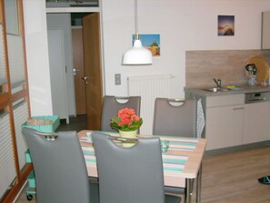 Una cocina compacta con comedor, que incluye una mesa con sillas, una lámpara colgante y una pequeña encimera con un lavabo y utensilios.