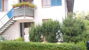 A two-story building with a white facade, blue shutters, and a wooden staircase leading to the entrance.