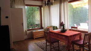 Un comedor con una mesa de madera, sillas y un banco. Hay una ventana con cortinas, techo de madera y una pequeña planta en el alféizar.