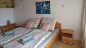 Un dormitorio con una cama, dos mesitas de noche, una mesilla, aire acondicionado instalado en la pared, una estantería con objetos decorativos y un cuadro.