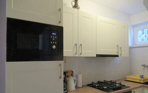 A kitchen with white cabinets, a black microwave, a gas stove, and a window with blinds.