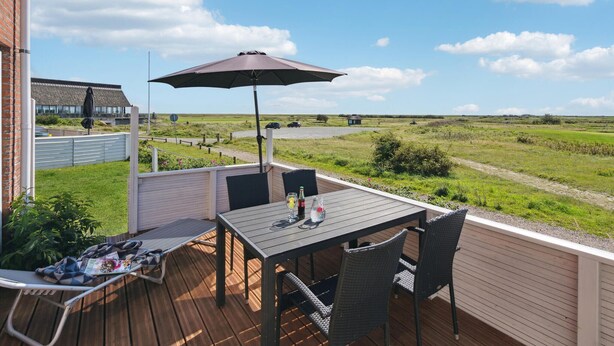 A wooden deck with a table and chairs, an umbrella, and a view of a rural landscape. - 3 bedroom lovely apartment in Rømø (Rømø)