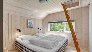 A bedroom with a large bed, a window with a view of trees, and wooden walls. - Nice home in Væggerløse with sauna (Væggerløse)