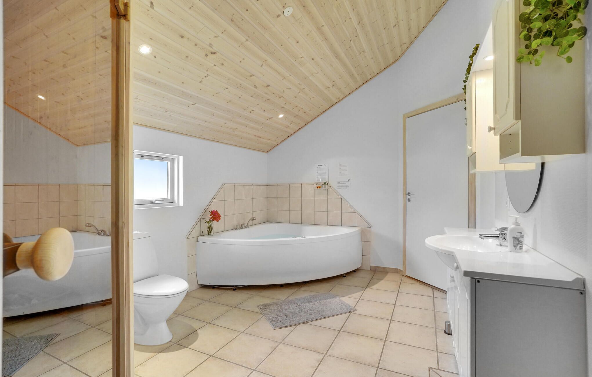 Een moderne badkamer met een houten plafond, een vrijstaand bad, toilet en een wastafel met spiegel erboven.