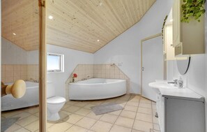 Et moderne badeværelse med træloft, et fristående badekar, toilet og vask med spejl over.