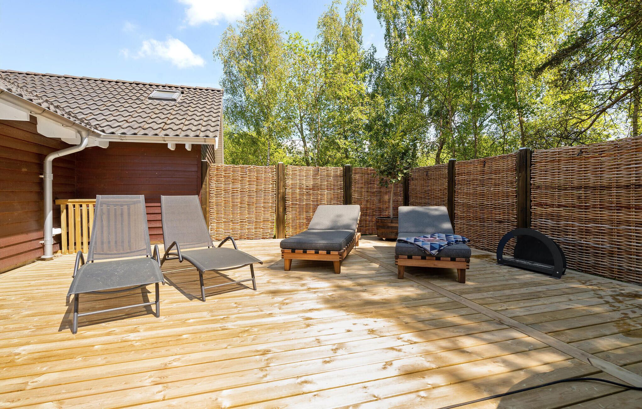 Une terrasse en bois avec des chaises longues et un barbecue.