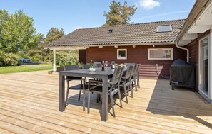 En udendørs træterrasse med spisebord og stole, grill og overdækket terrasse.