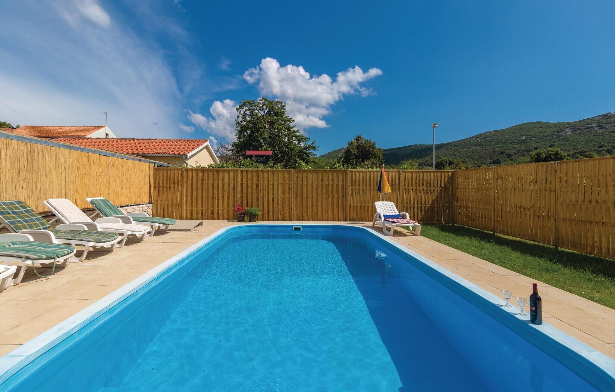 Une piscine rectangulaire avec une terrasse en bois, entourée d’une clôture en bois, et une rangée de chaises longues d’un côté.
