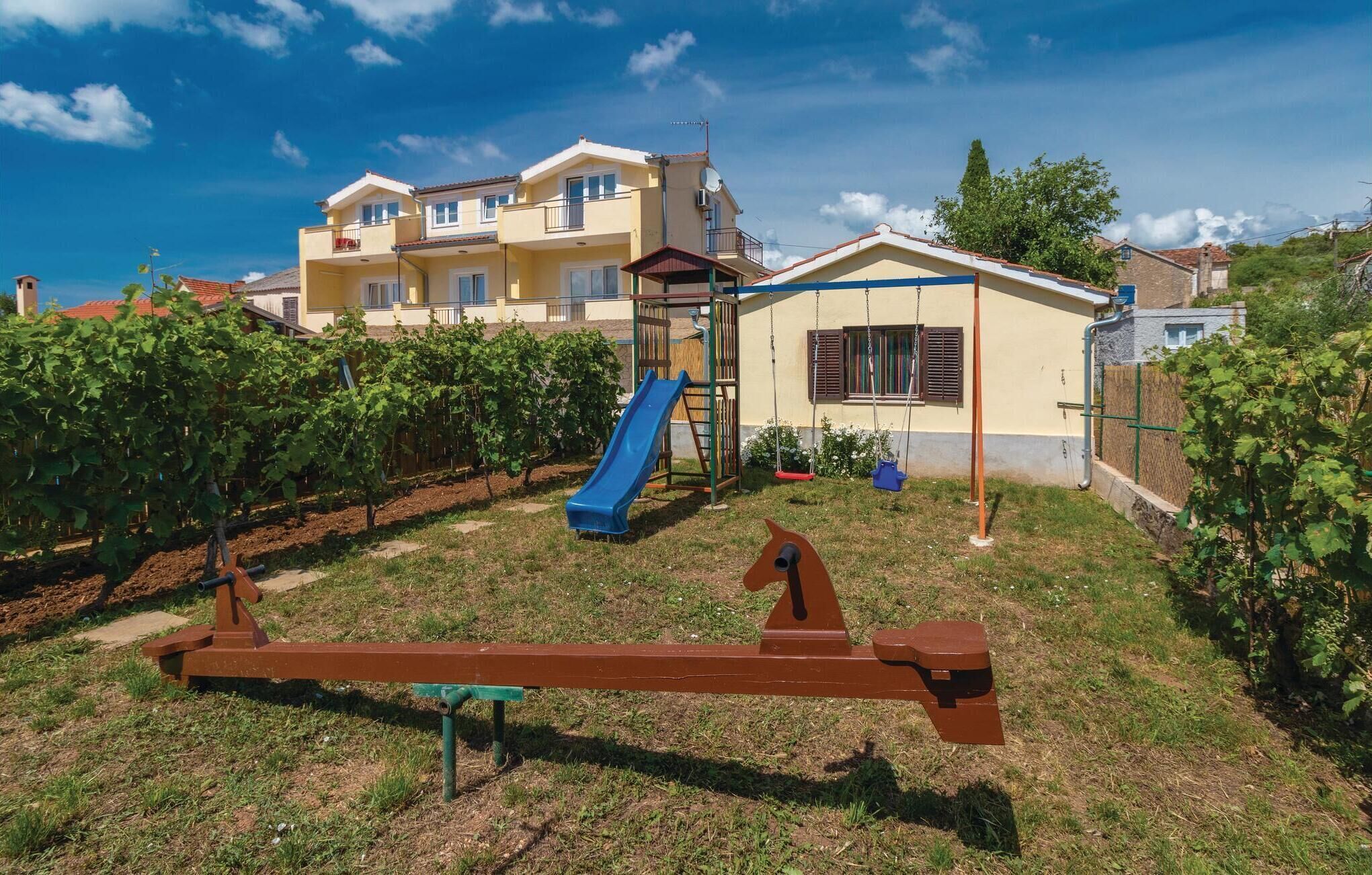 A residential building with a playground, including a slide and swings, surrounded by a vineyard.