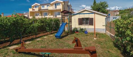 A residential building with a playground, including a slide and swings, surrounded by a vineyard.