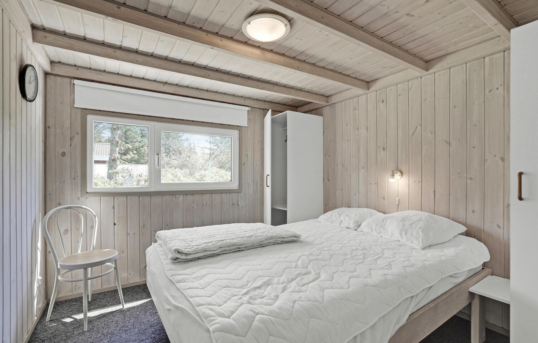 Un dormitorio con cama, una silla, un armario y una ventana.