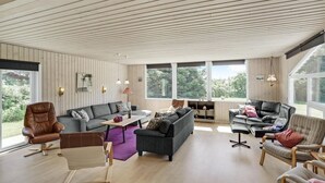 A spacious living room with a high ceiling, large windows, and a variety of seating options including a sofa, chairs, and a coffee table. - Awesome home in Løkken with sauna (Løkken)
