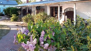Ein Haus mit überdachter Veranda, einem Garten mit Fliederbüschen und einem Pflasterweg.