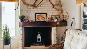 Ein gemütliches Wohnzimmer mit Kamin aus Backstein, einem weißen, gepolsterten Sofa und einem Korbstuhl.