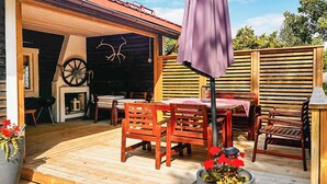 Eine Holzterrasse im Freien mit Tisch und Stühlen, einem violetten Sonnenschirm und Kübelpflanzen.