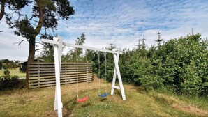 A swing set in a backyard with a wooden fence and dense shrubbery. - 5 bedroom nice home in Væggerløse (Væggerløse)