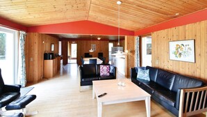 A cozy cabin interior with a wooden ceiling, a dining area, a living room with a sofa and coffee table, and a kitchen area. - 5 bedroom nice home in Væggerløse (Væggerløse)