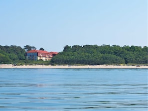 Ein Hotel direkt am Strand mit mehreren Stockwerken, einem roten Dach und Blick auf den Strand und das Wasser.