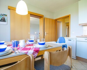 En matplats med ett bord dukat för två personer, en blå stol och ett köksområde med diskmaskin.
