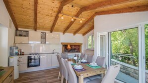 Een moderne keuken met houten balken, een open haard en een eethoek met een groot raam met uitzicht op groen.