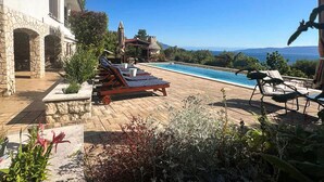 A poolside area with lounge chairs, a stone building, and a view of the sea.