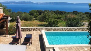 A pool with a stone wall, lounge chairs, and a view of the sea.