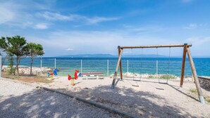 A playground with swings and a bench, a fenced area, and a view of the sea.