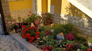 A garden with various potted plants and flowers, a stone pathway, and a yellow building with a white door. - 2 bedroom amazing apartment in Rabac (Rabac)