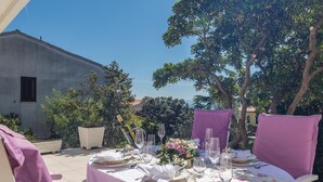 An outdoor dining area with a table set for two, surrounded by trees and a building in the background. - 2 bedroom amazing apartment in Rabac (Rabac)