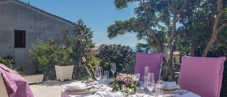 An outdoor dining area with a table set for two, surrounded by trees and a building in the background.