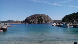 A coastal scene with clear blue water, a rocky island, and boats docked at a pier. - 3 bedroom awesome home in Lyngdal (Lyngdal)