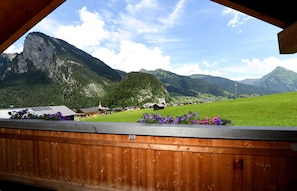 Vista de la montaña desde un balcón de madera, con casas y otra montaña al fondo.