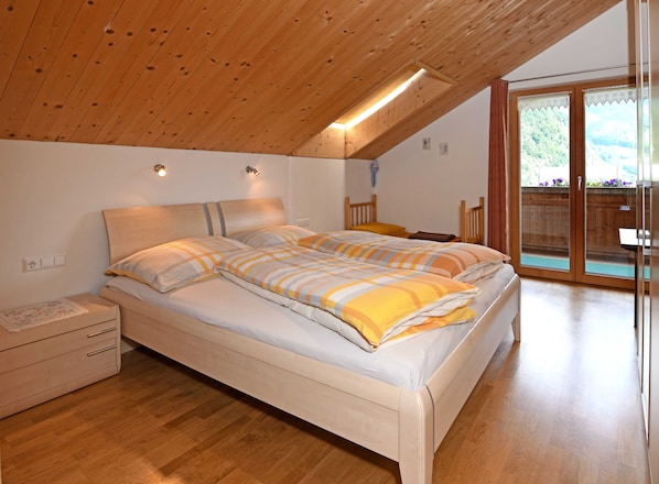 Une chambre avec un plafond en bois, un lit avec une literie à rayures, une table de chevet et une porte-fenêtre coulissante donnant sur un espace extérieur.