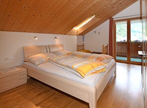 Un dormitorio con techo de madera, cama con ropa de cama a rayas, mesita de noche y puerta corredera de vidrio que da a un espacio exterior.