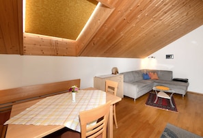 Un espacio tipo loft con techo de madera, una mesa de comedor con sillas, un sofá y una pequeña mesita auxiliar.
