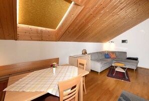 Un espacio tipo loft con techo de madera, una mesa de comedor con sillas, un sofá y una pequeña mesita auxiliar.