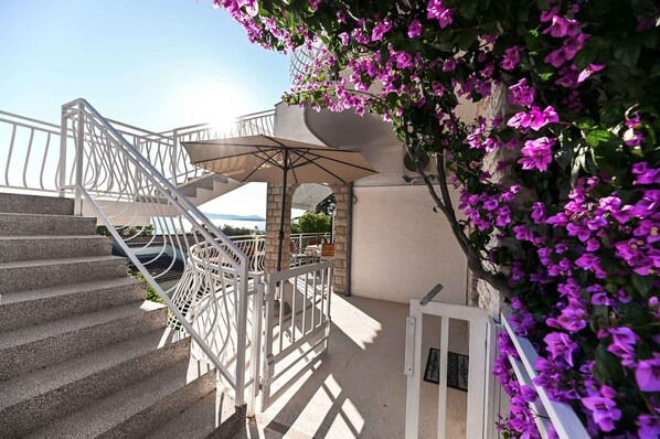 Eine Treppe mit Metallgeländer, ein überdachter Außenbereich zum Sitzen und eine Wand, die mit violetten Blumen geschmückt ist.