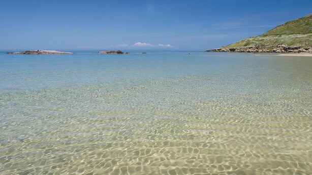 A clear, shallow coastal water body with rocky outcrops and a distant landmass.