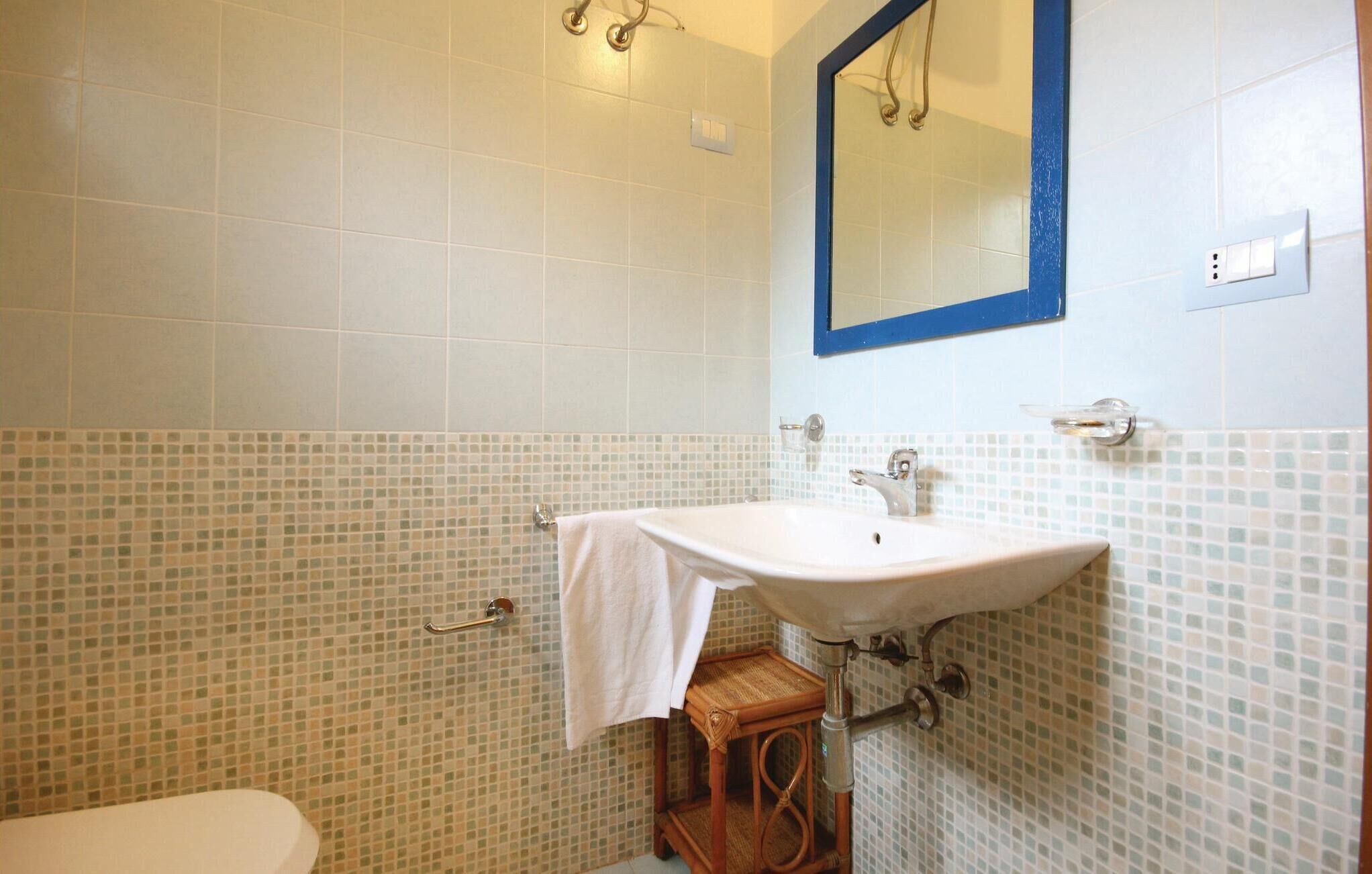 Une salle de bain avec un lavabo blanc, un miroir avec un cadre bleu et un mur recouvert de mosaïques.