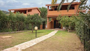 A pathway leading to a building with a tiled roof and a small garden area with a lamp post.