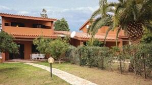 A two-story building with a tiled roof, surrounded by a well-maintained garden with palm trees and a stone pathway leading to the entrance.
