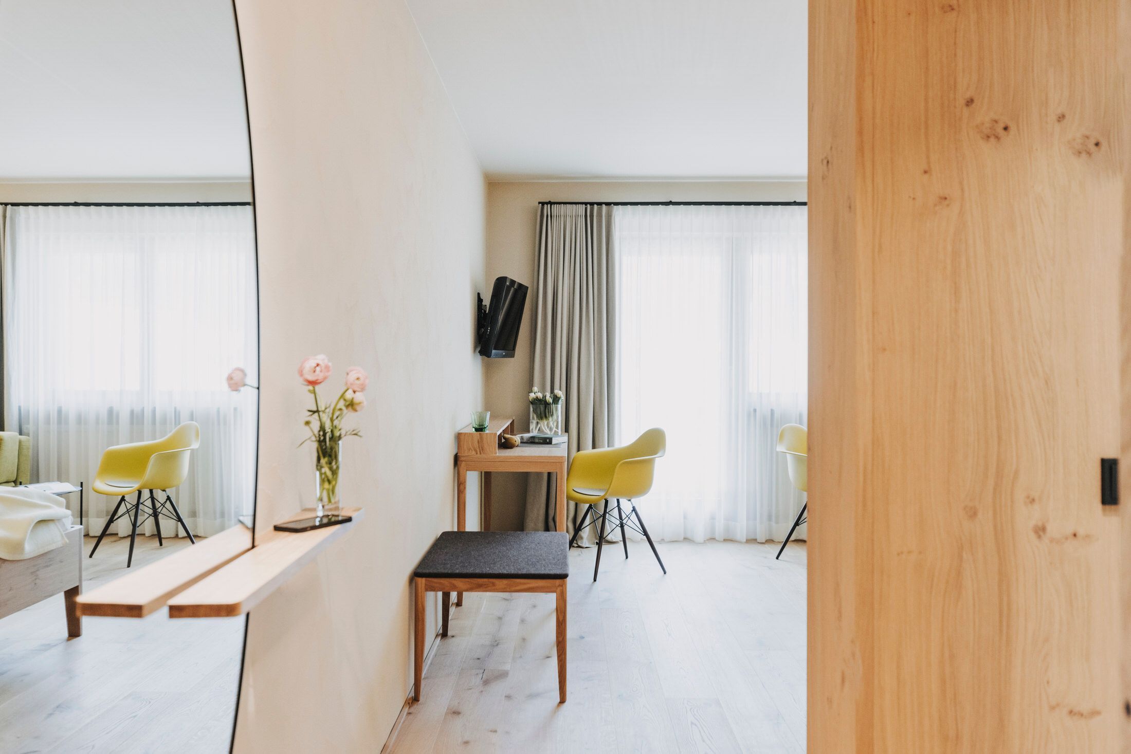 A modern room with a wooden bench, two yellow chairs, a small table, and a mirror.